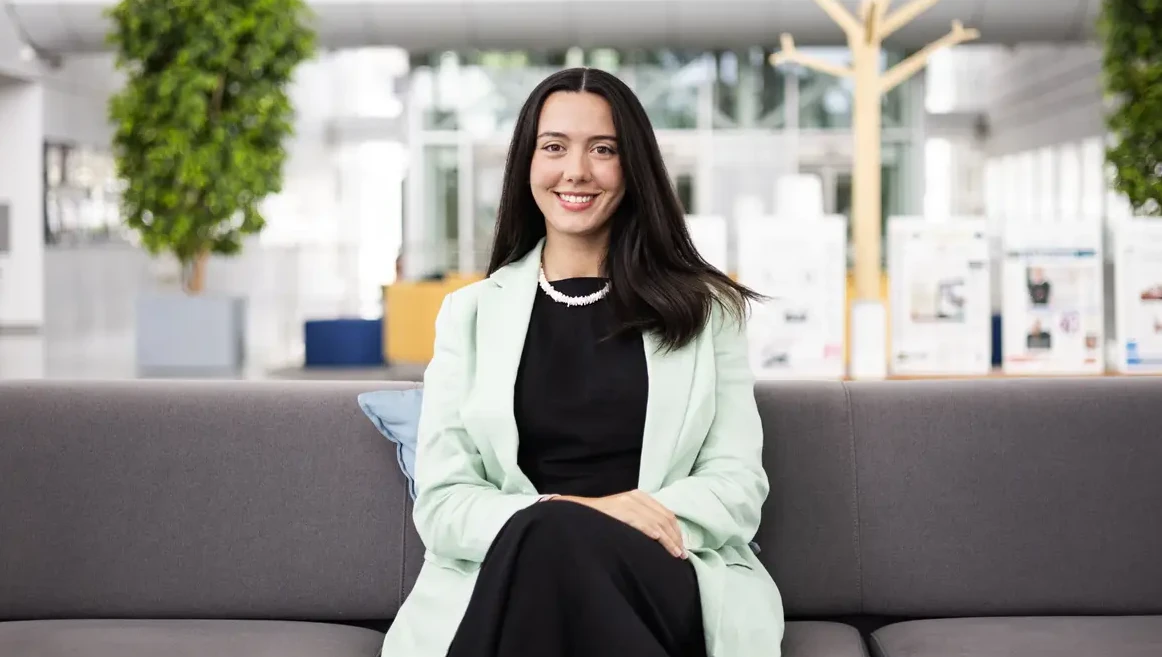 Foto da Leonor Caldeira. A Leonor aparece sentada num sofá, a olhar directamente para a camera, com um sorriso confiante e um blazer menta, num escritório open space.